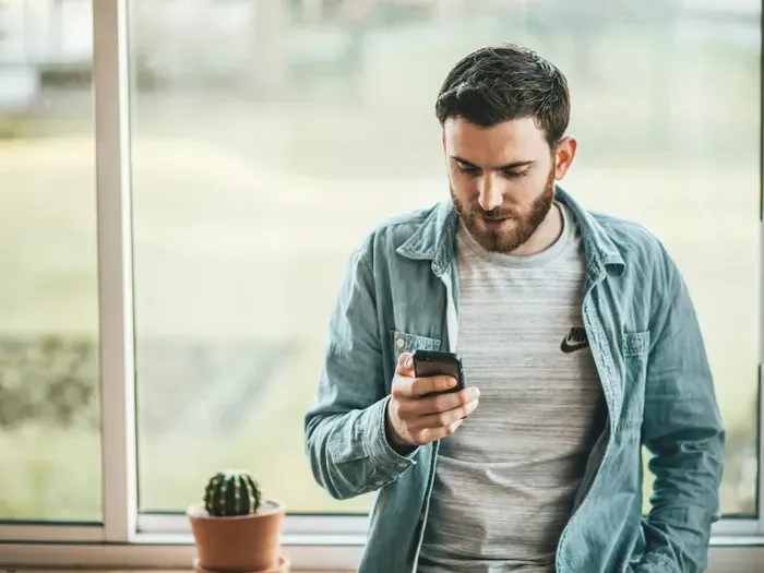 Young entrepreneur checks his smartphone by a window, managing listings and leads on Local Biz Network Hub